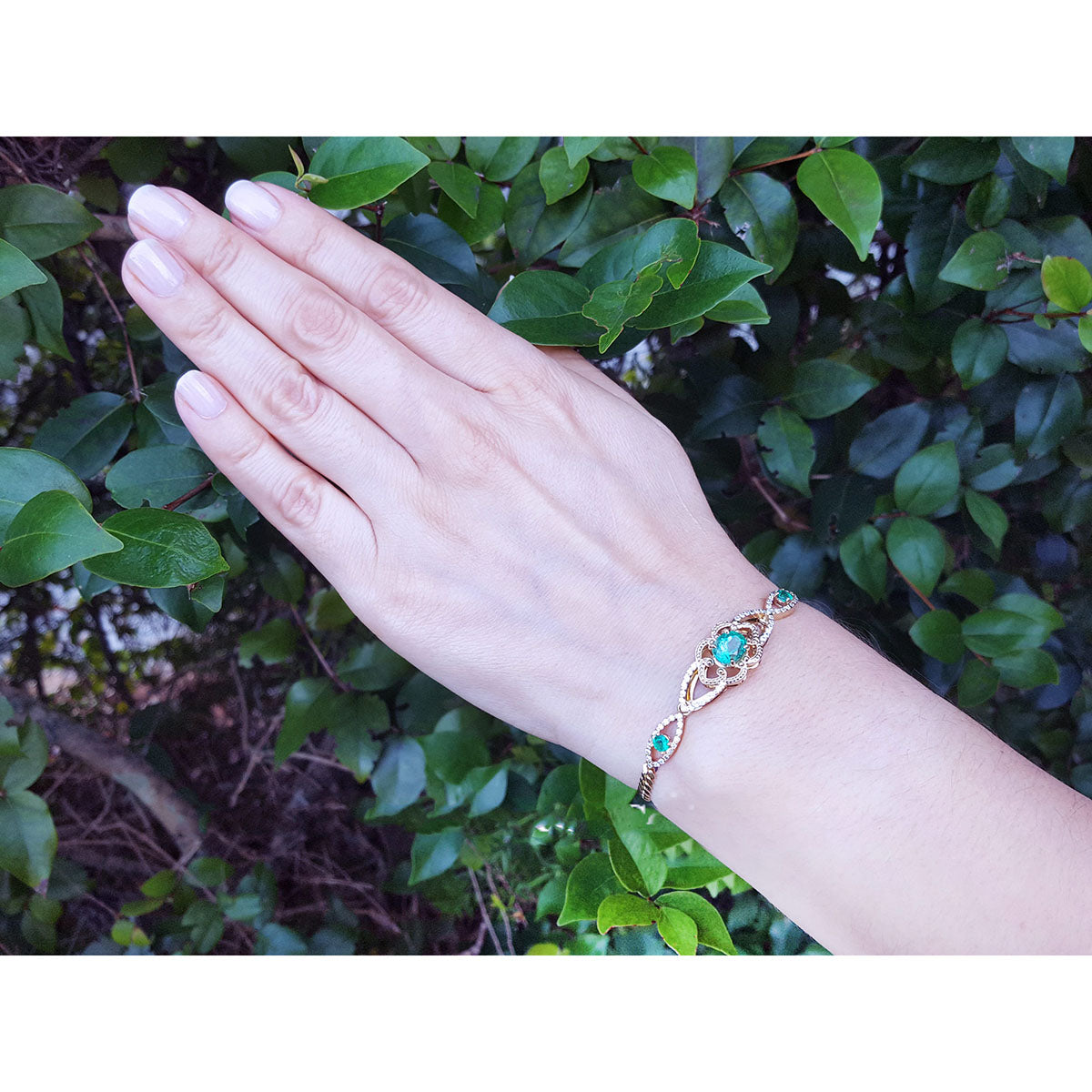 A woman&#39;s hand wearing a bracelet with Muzo colombian emeralds against a leafy background.
