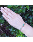 A woman's hand wearing a bracelet with Muzo colombian emeralds against a leafy background.