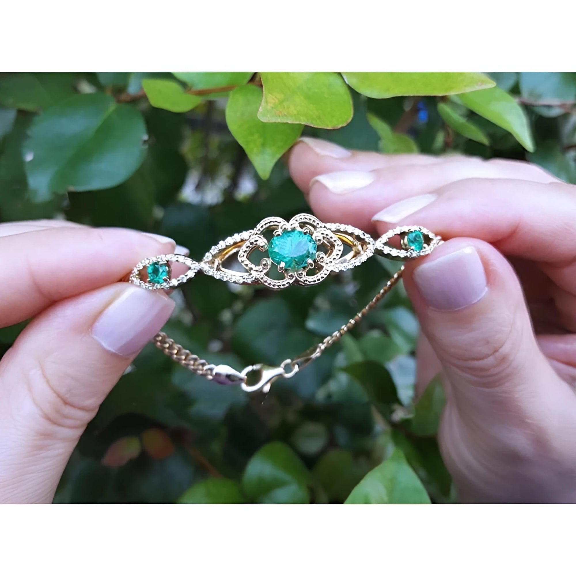 Vintage 14K yellow gold bracelet with oval emeralds and diamonds, held against green leaves.