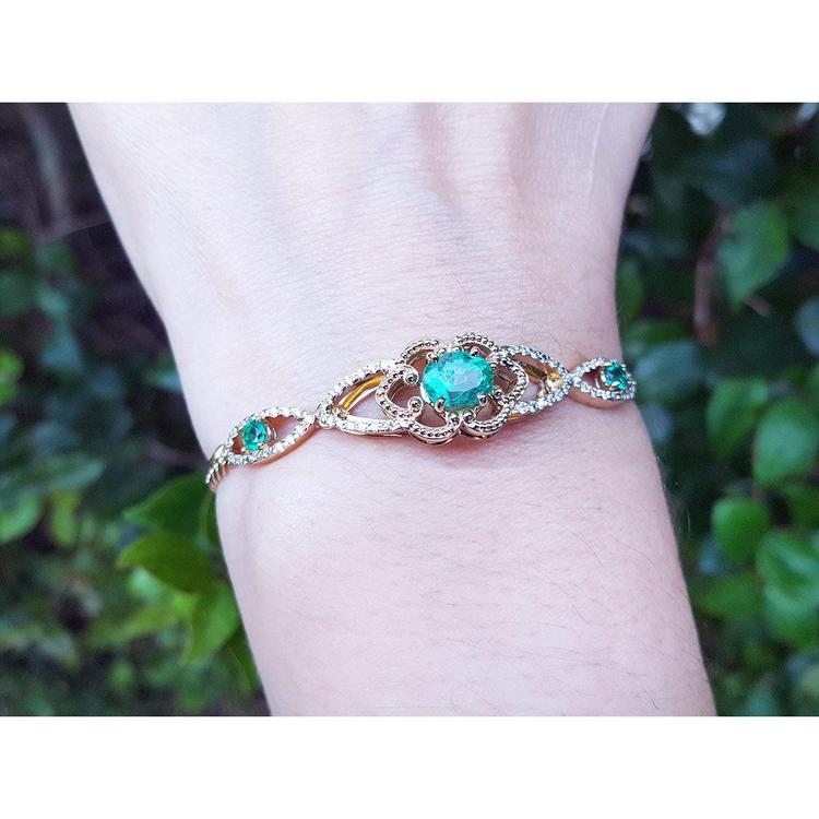 A women's bracelet with an oval cut natural colombian emerald and accent diamonds in 14k gold.