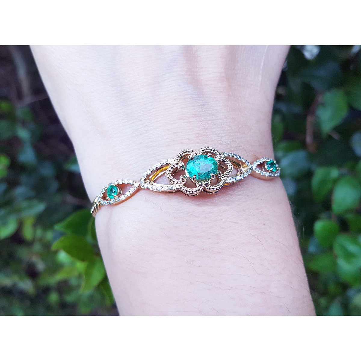 Bracelet with an oval cut natural colombian emerald on a wrist against a blurred green background.