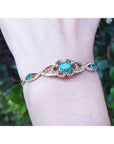 Bracelet with an oval cut natural colombian emerald on a wrist against a blurred green background.