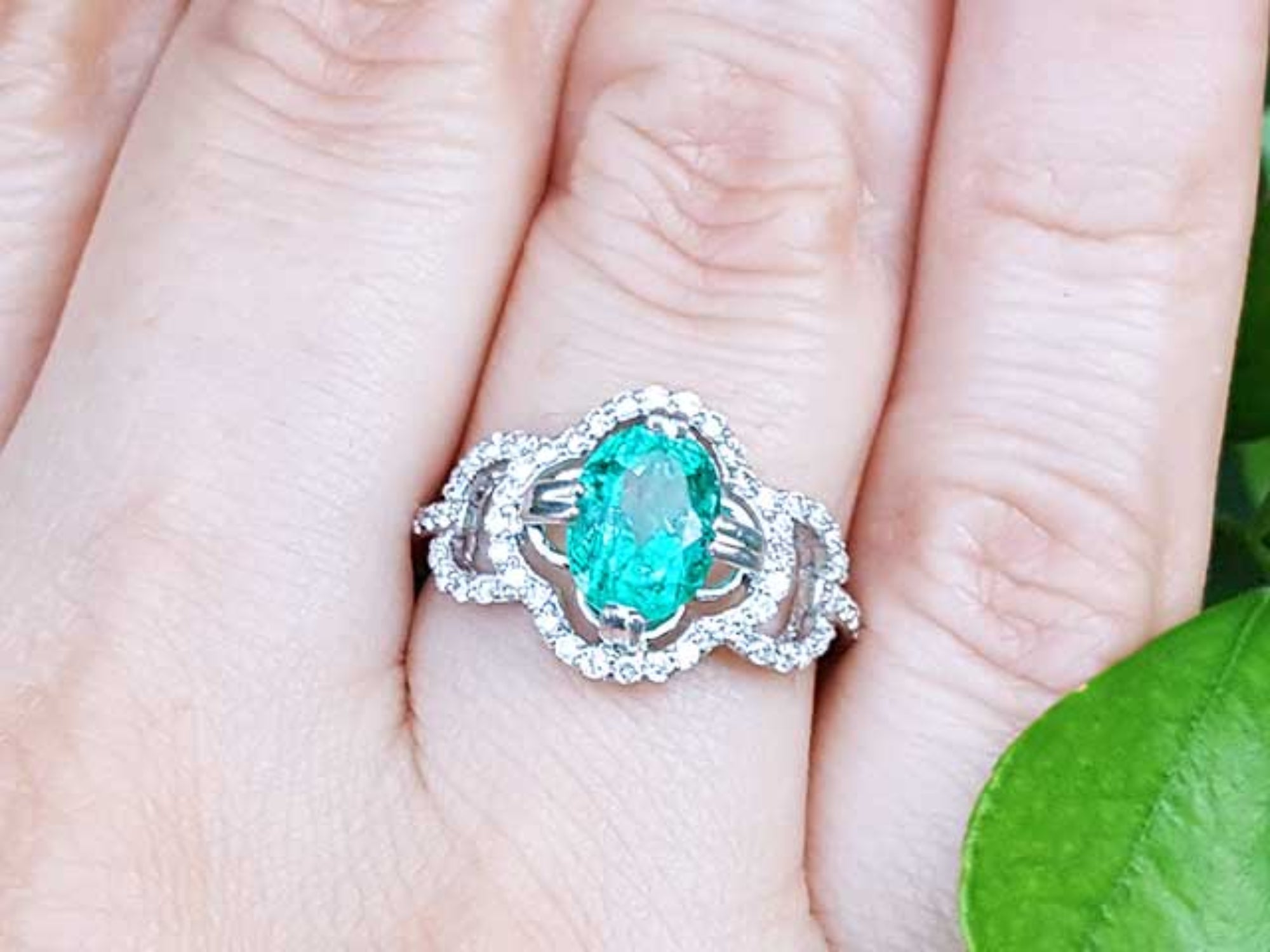Clover ring with an oval cut emerald on a person's finger against a natural background.