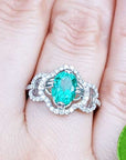 Clover ring with an oval cut emerald on a person's finger against a natural background.