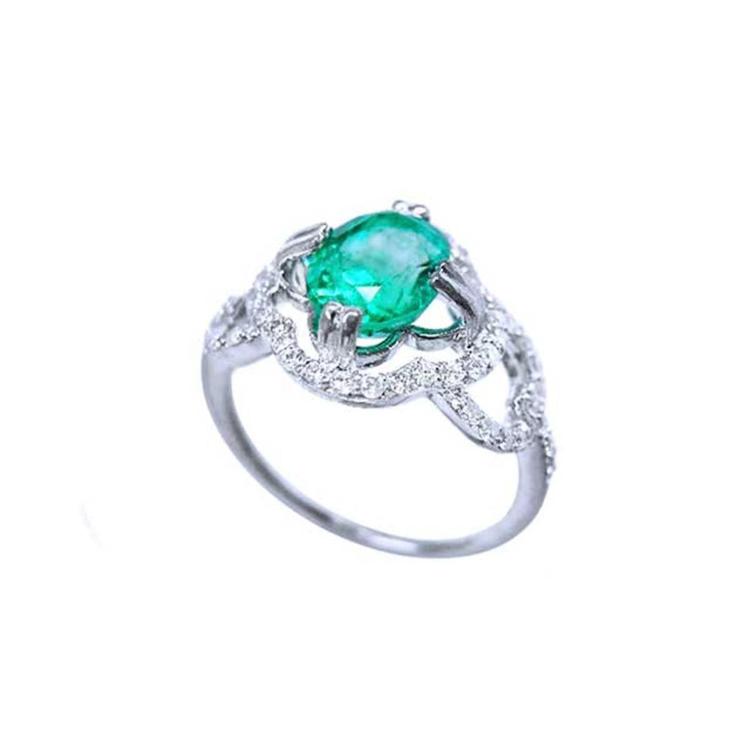 A detailed view of an oval cut emerald centered in a clover ring design adorned with diamonds.