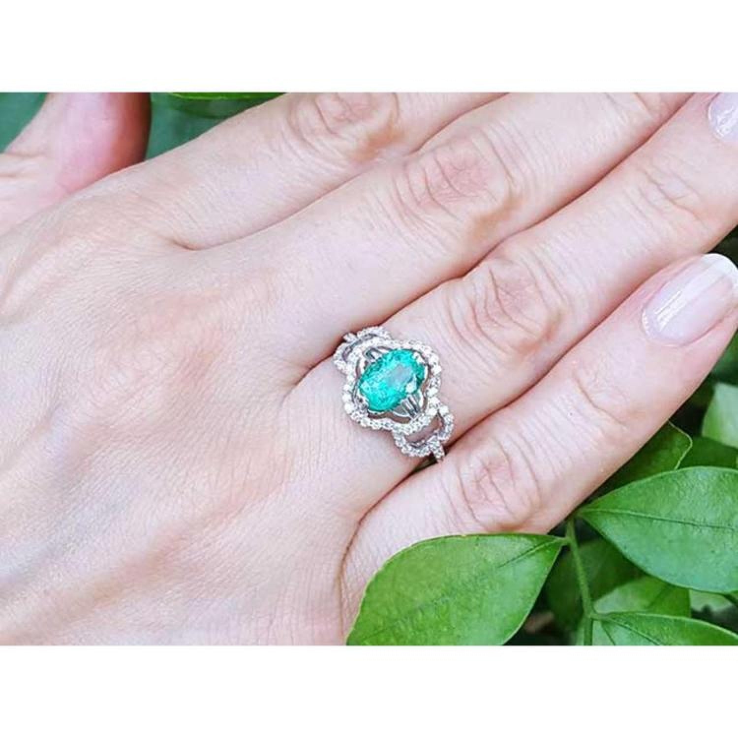 Oval emerald clover ring with diamond halo in 14K white gold on a hand.