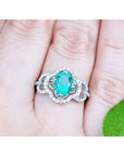 Clover 14k white gold ring with an oval cut natural colombian emerald on a person's finger.
