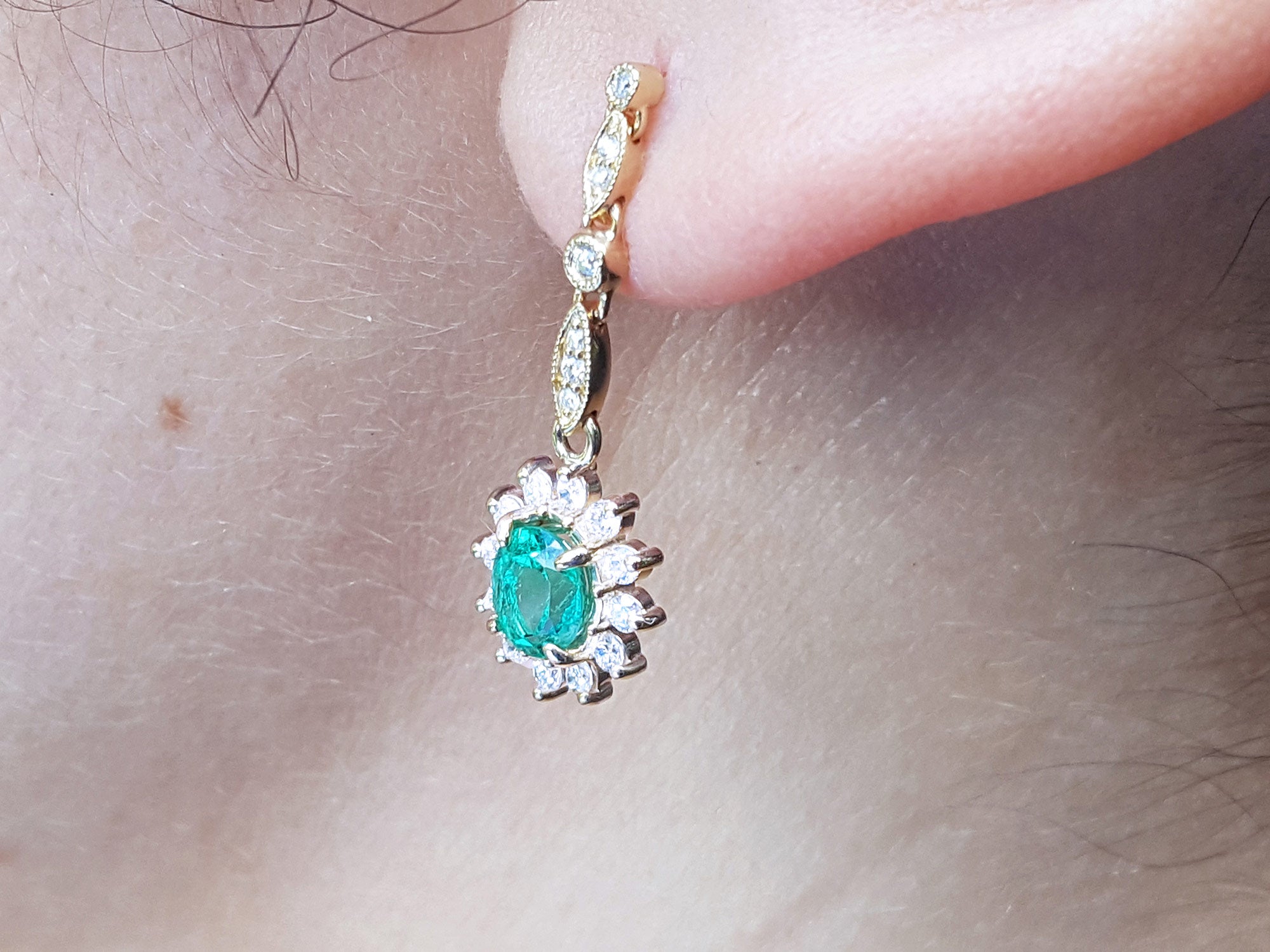Close-up of a gold earring with an oval cut emerald yellow gold on a person&#39;s ear.