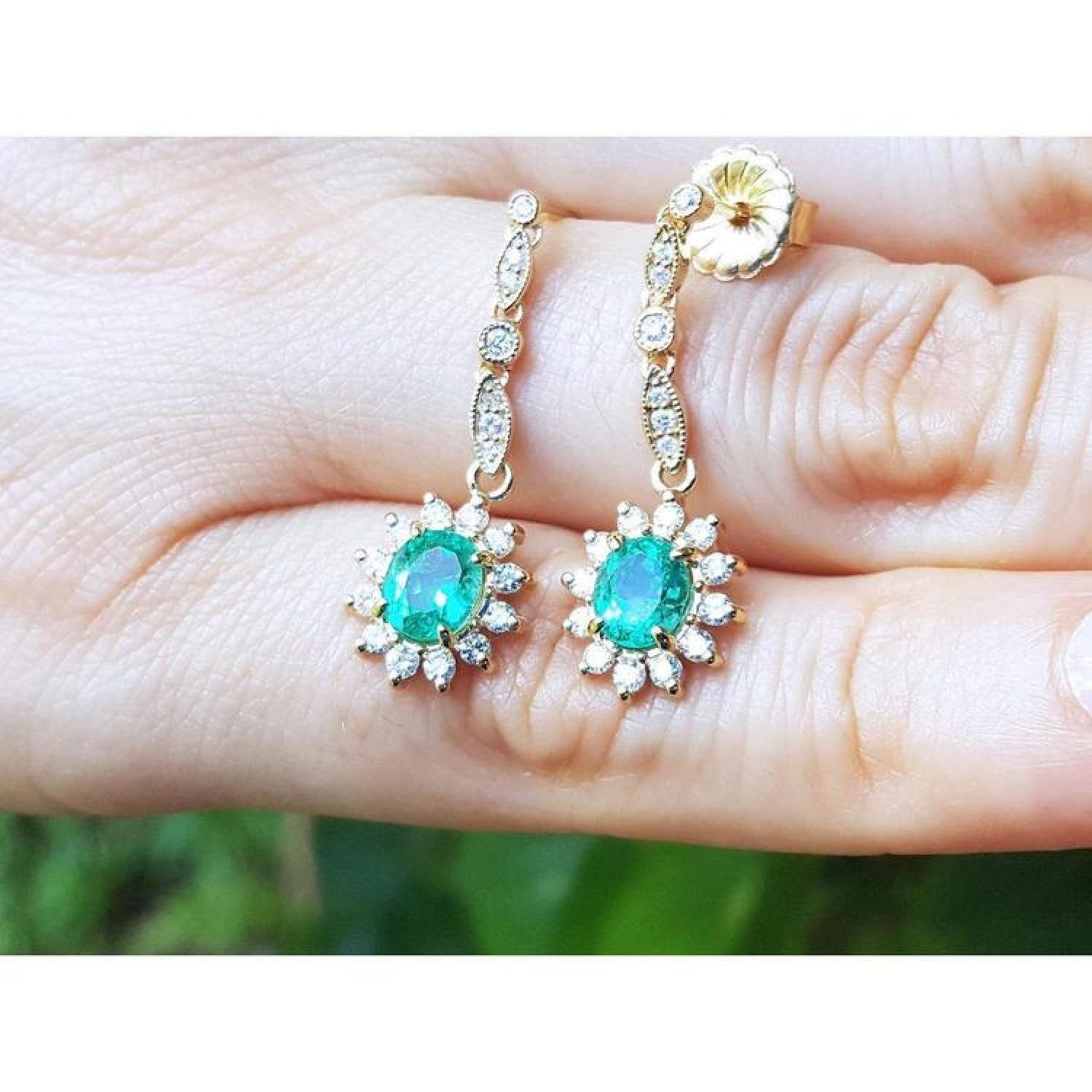 14K yellow gold dangle earrings with oval emeralds and diamond halo.