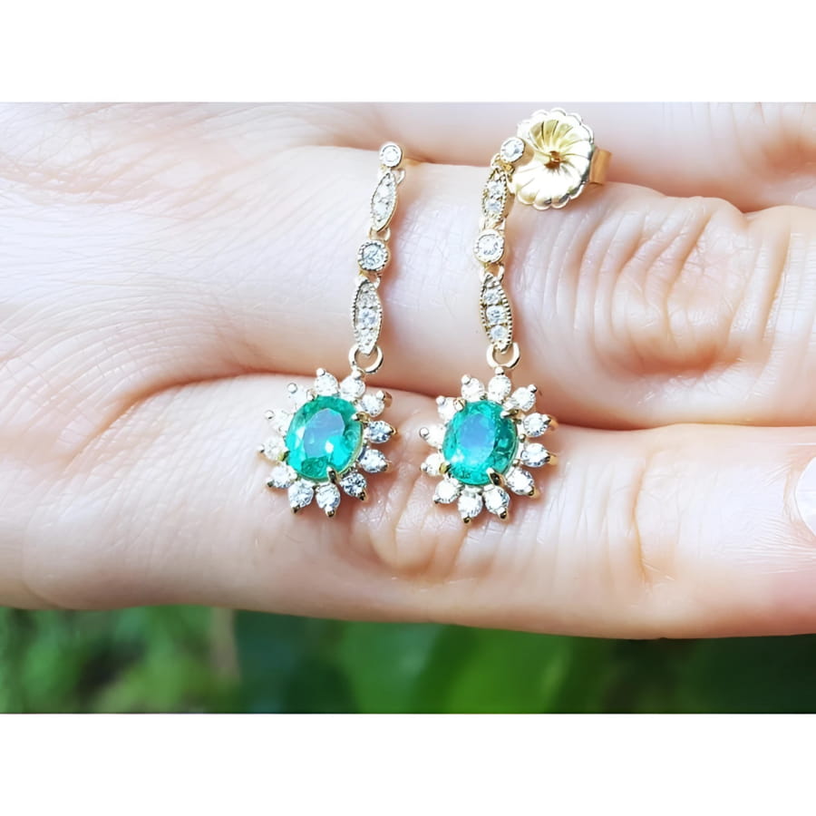 14K yellow gold dangle earrings with oval emeralds and diamond halo.