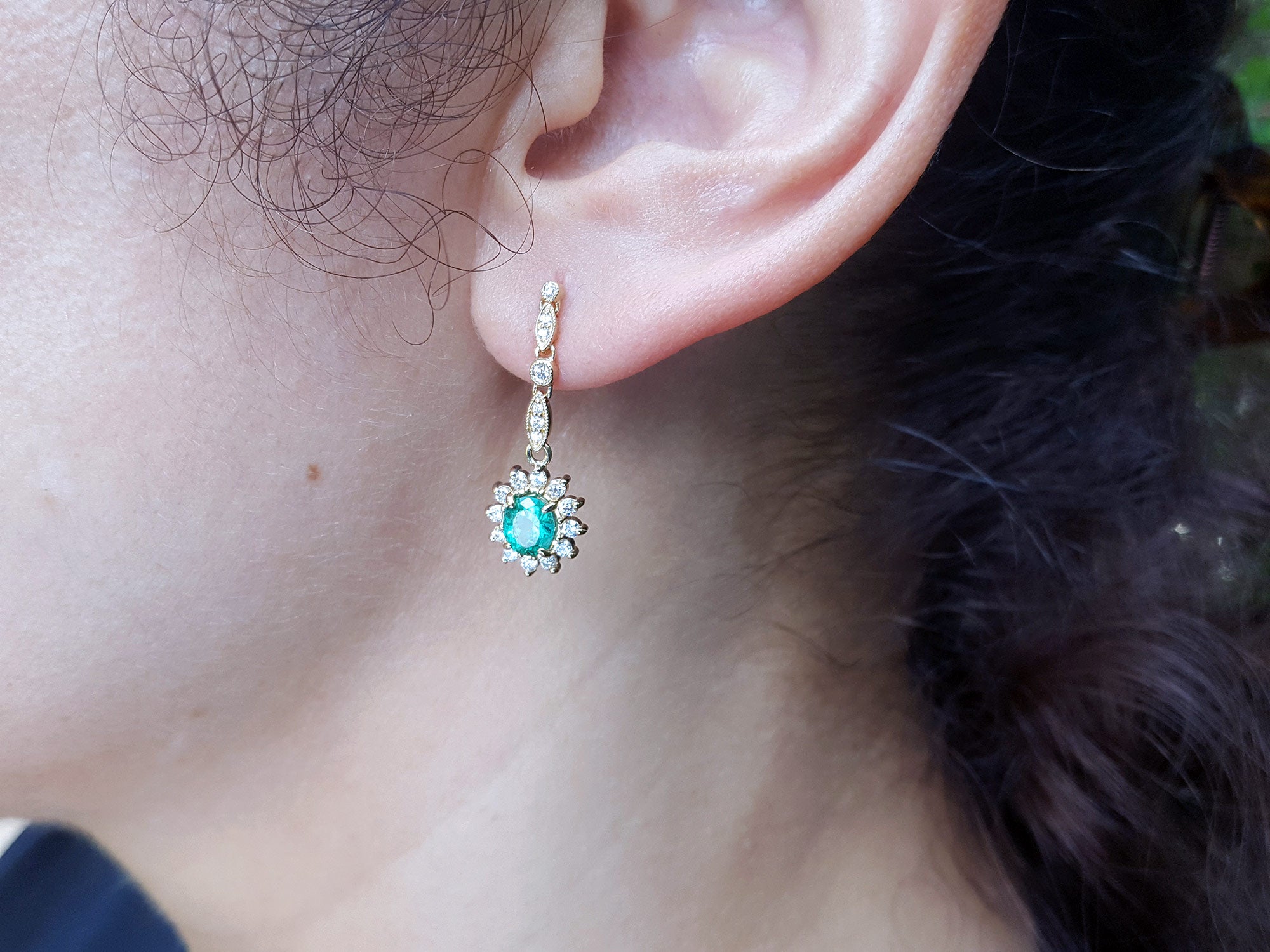 Close-up of an ear wearing a diamond and emerald earring oval cut halo diamond.