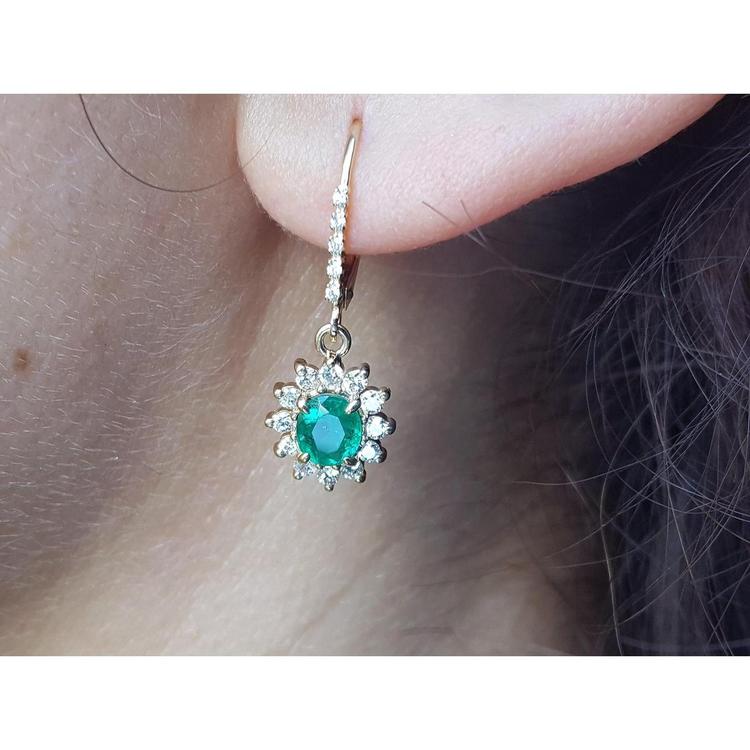 Close-up of a halo diamond oval cut emerald earrings lever backs worn on a woman's ear.