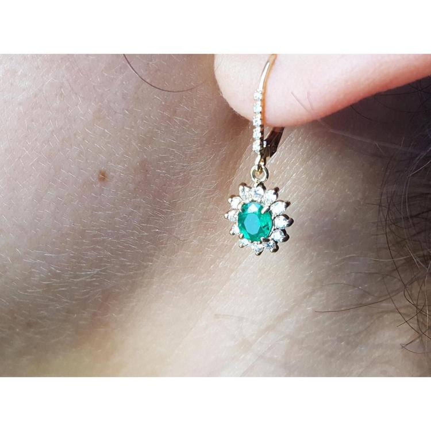 14K gold oval cut emerald earrings with diamond halo and lever backs on an ear.