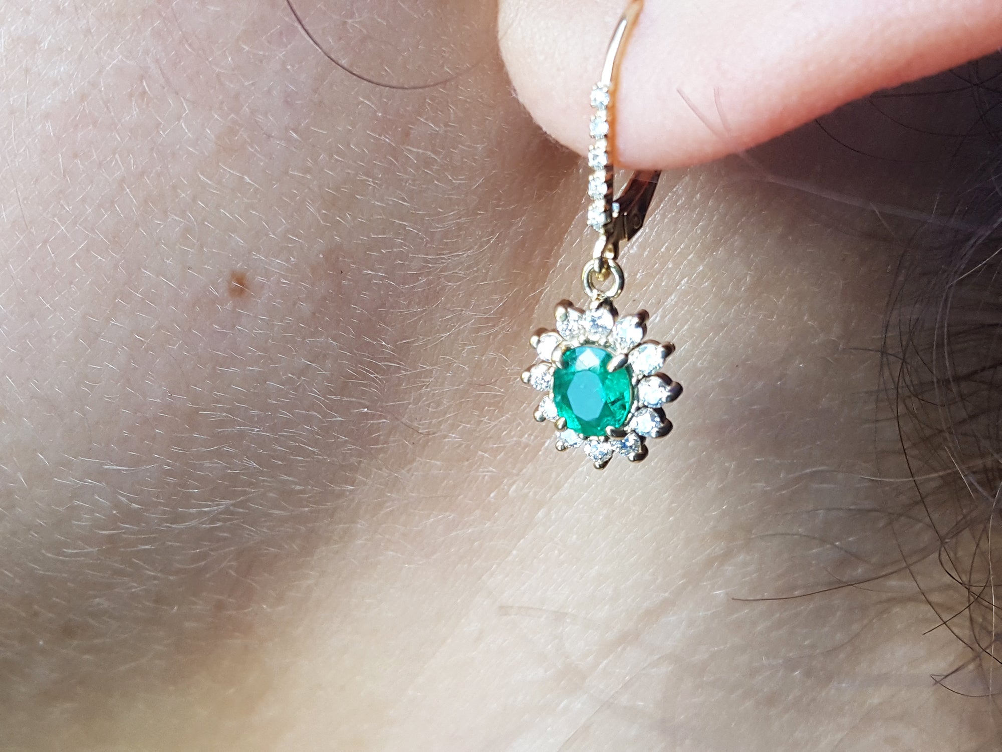 Close-up of a gold earring with a natural emerald oval cut, lever back dangling from an earlobe