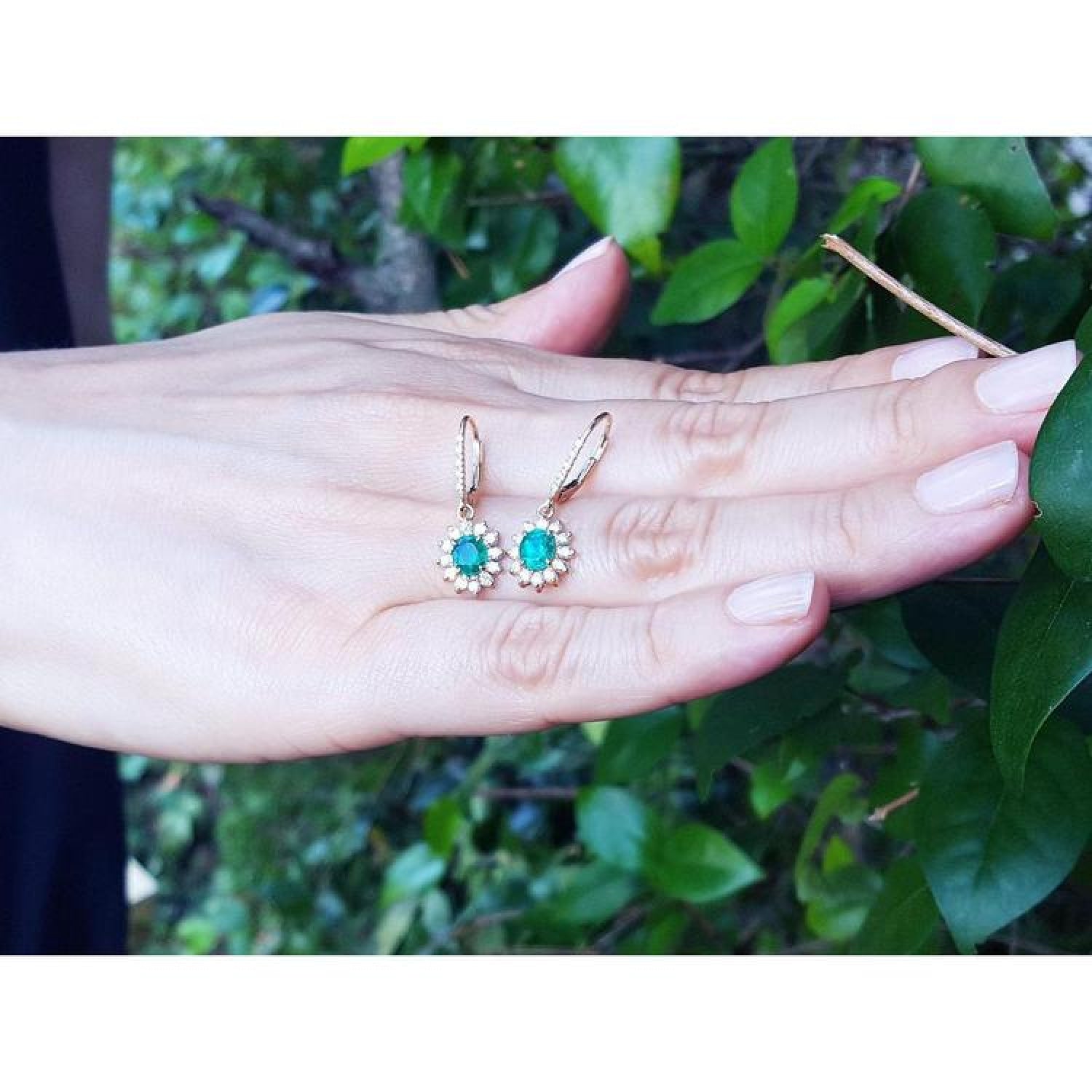 1.09 carat oval cut Colombian emerald and diamond halo earrings in 14K gold with lever backs.