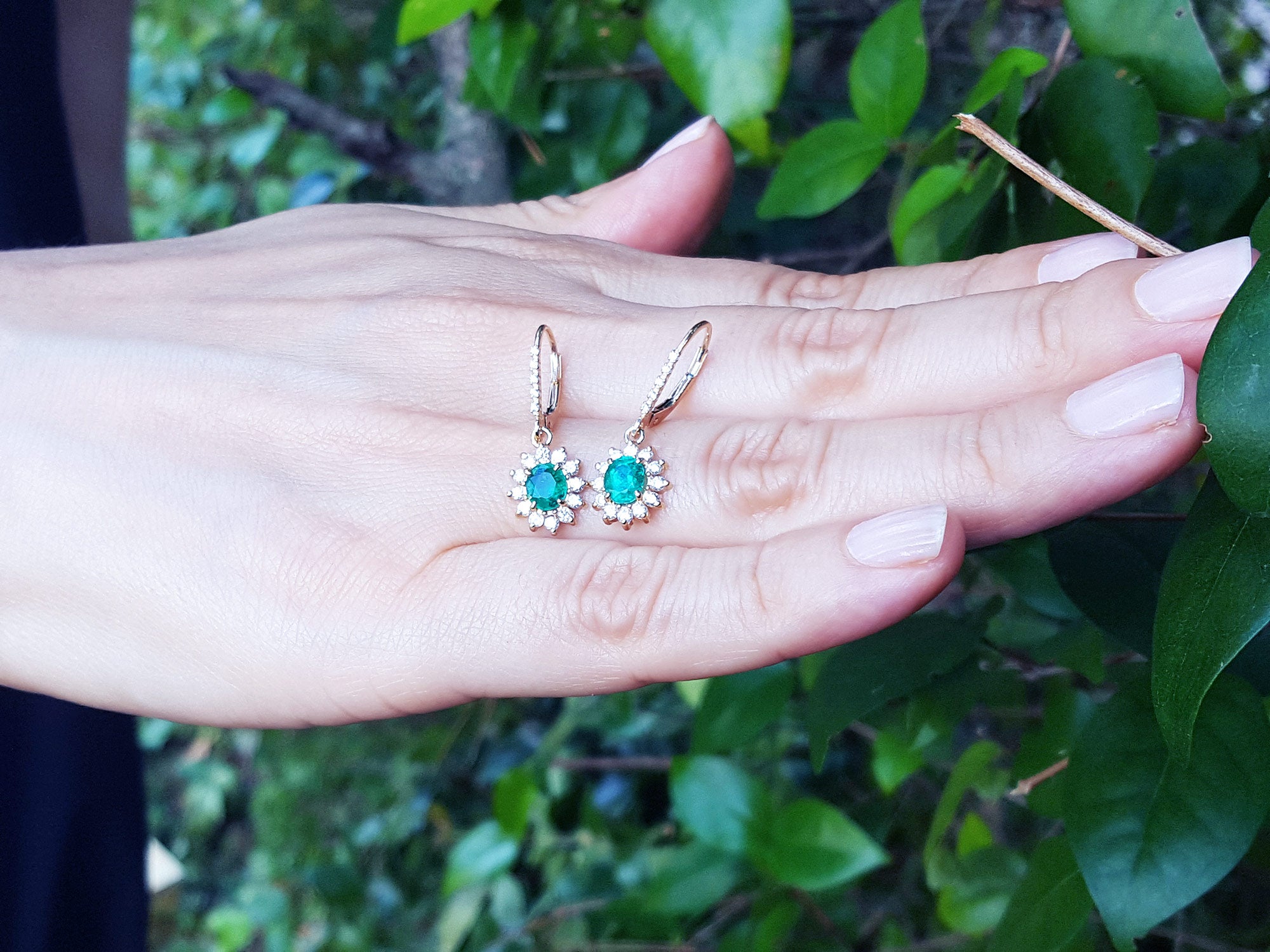 emerald earrings held in a hand with a green leafy background