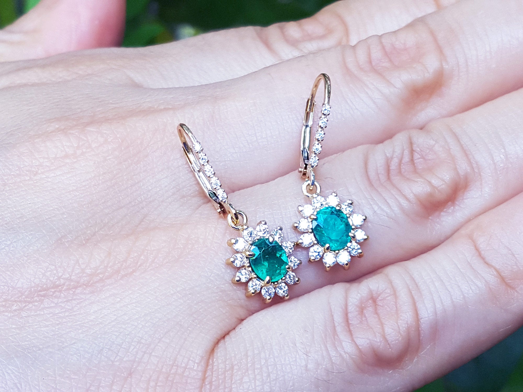Pair of emerald oval cut gemstone earrings with halo diamond on a hand