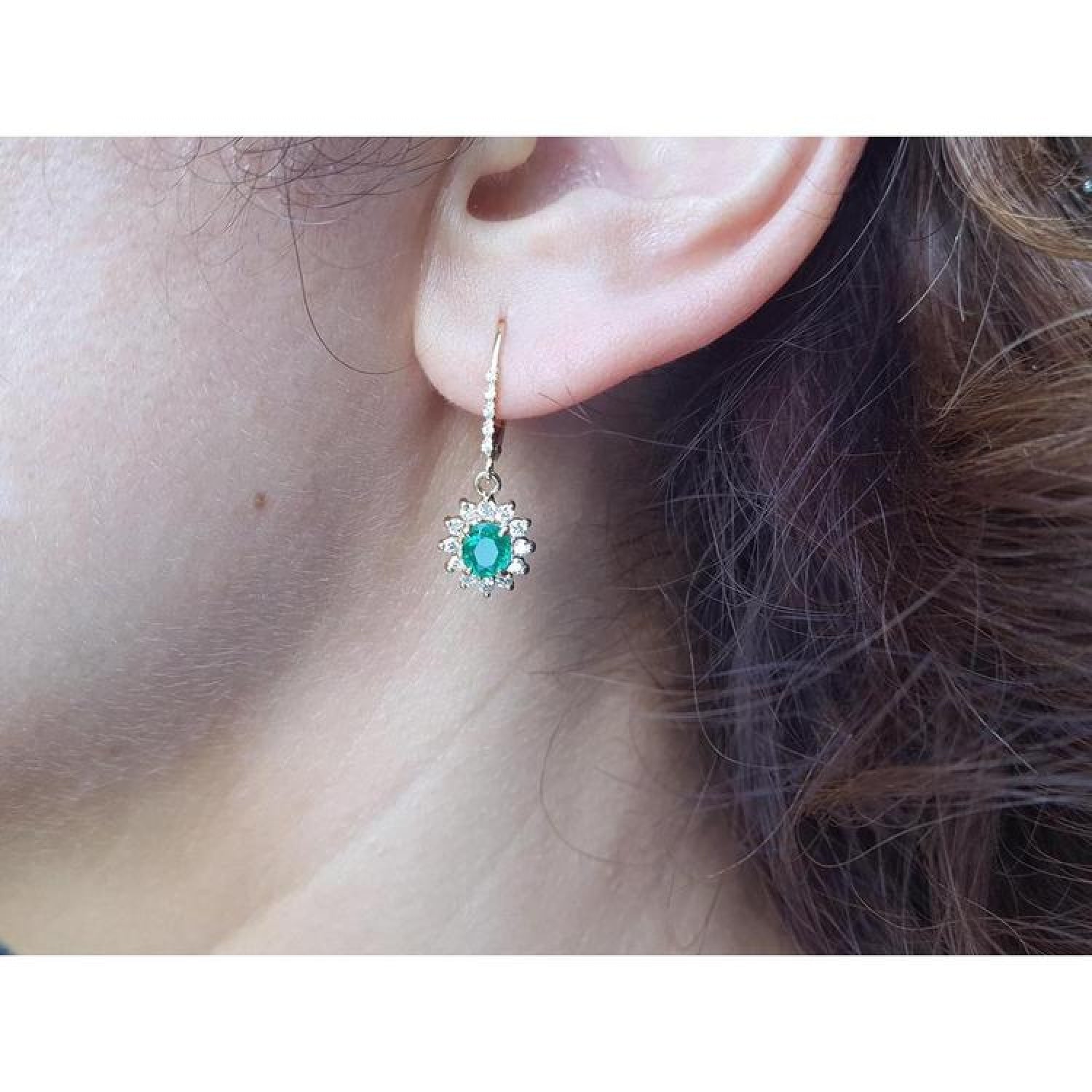 14K gold oval cut emerald earrings with diamond halo and lever backs on an ear.