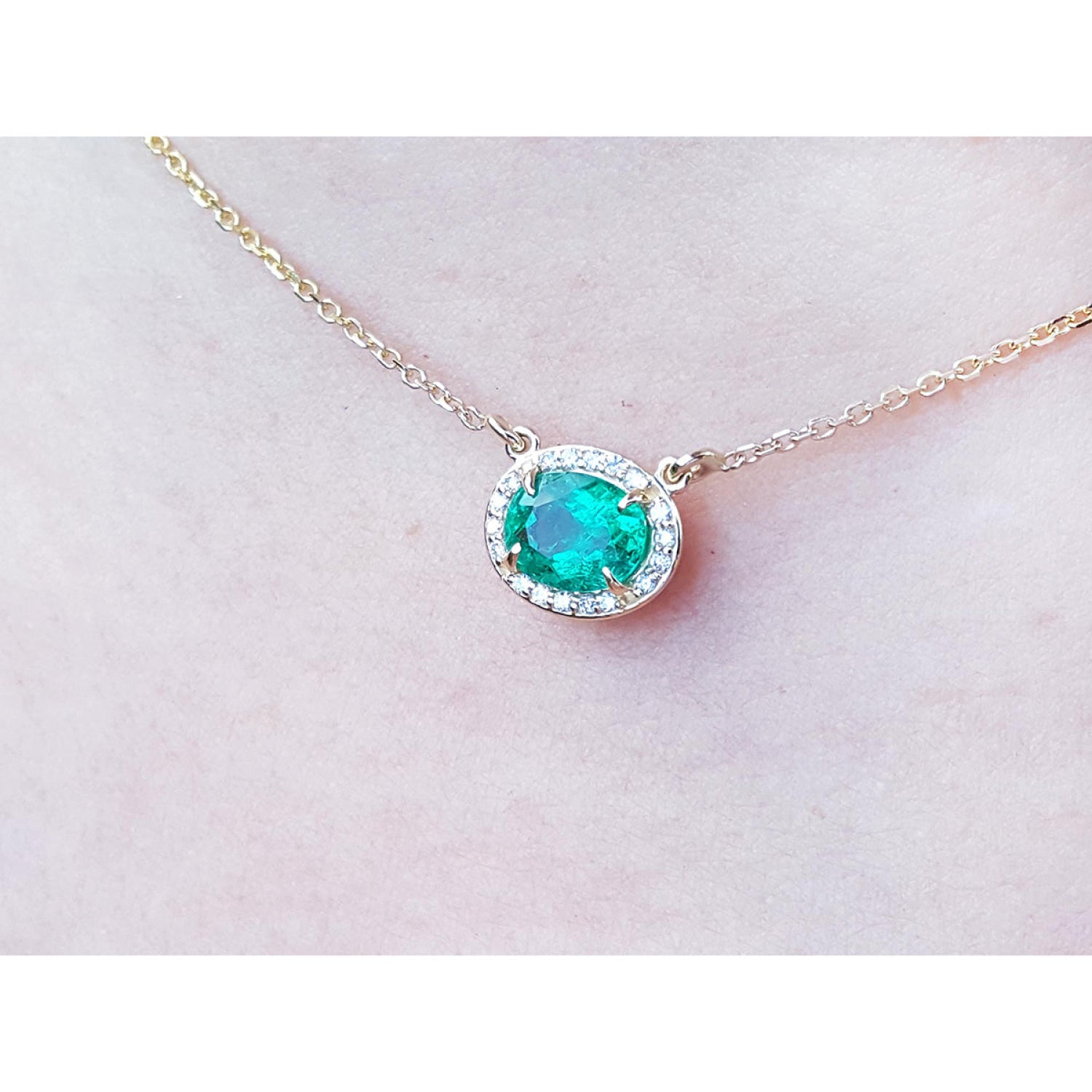 Oval Muzo emerald necklace with diamond halo on a delicate 14K yellow gold chain.