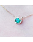 Oval Muzo emerald necklace with diamond halo on a delicate 14K yellow gold chain.