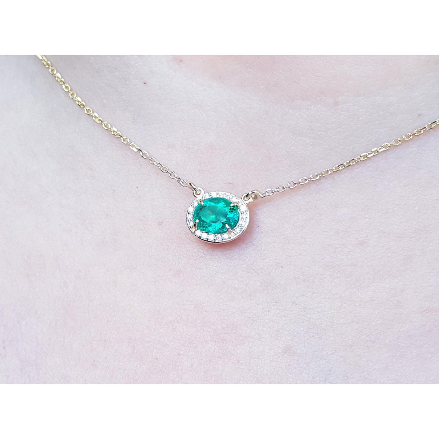 Oval Muzo emerald necklace with diamond halo on a delicate 14K yellow gold chain.