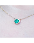 Oval Muzo emerald necklace with diamond halo on a delicate 14K yellow gold chain.