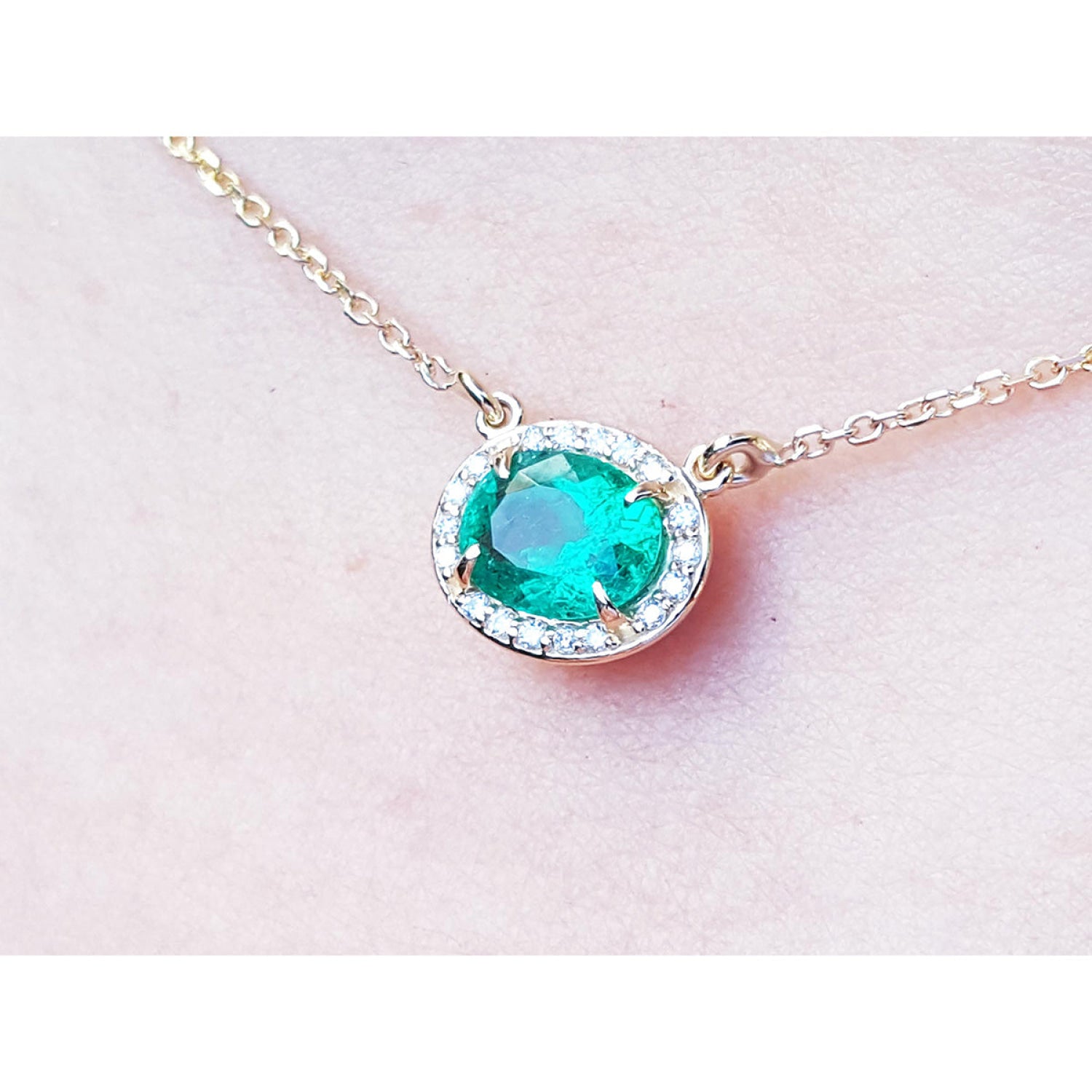0.90 carat oval Muzo emerald necklace with diamond halo on a 14K yellow gold chain.