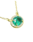 Oval Muzo emerald necklace with diamond halo on 14K yellow gold chain.