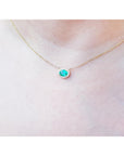 Oval Muzo emerald necklace with diamond halo on a delicate 14K yellow gold chain.