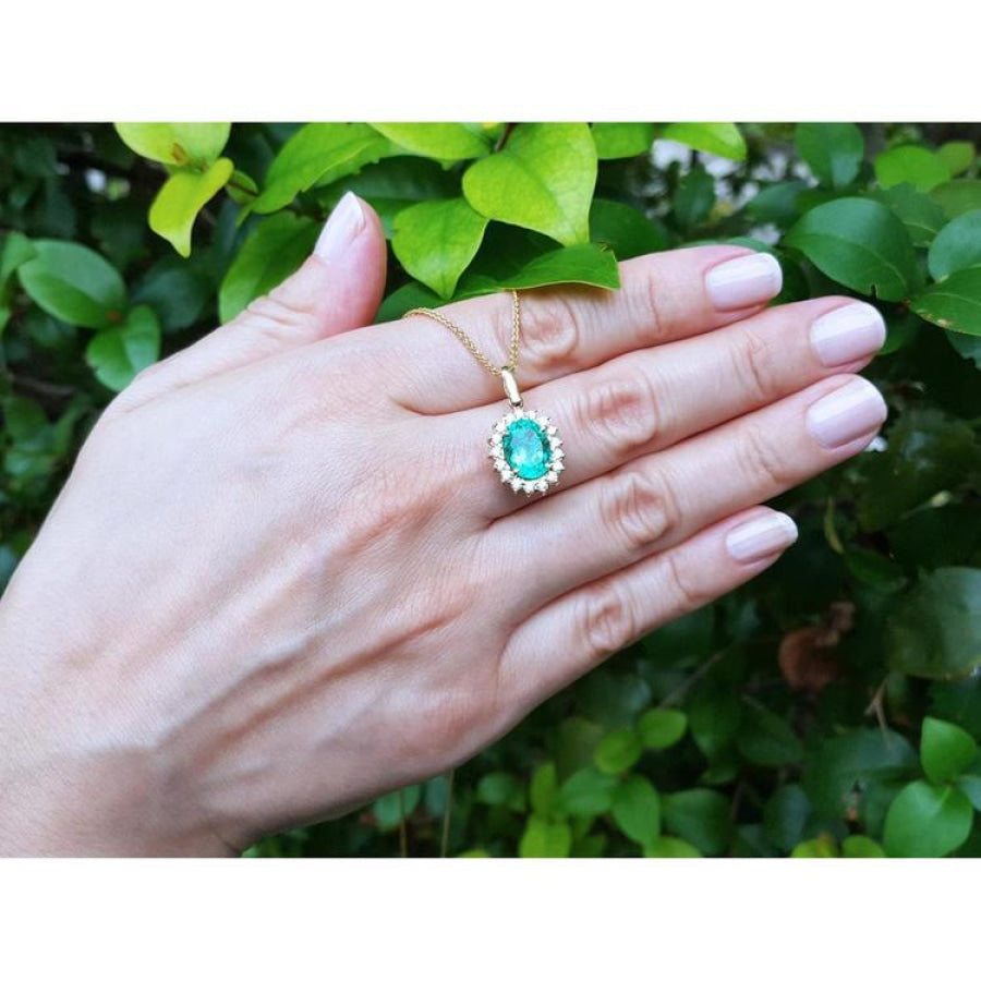 Oval natural emerald pendant with halo diamonds in 18K yellow gold, worn on a hand.