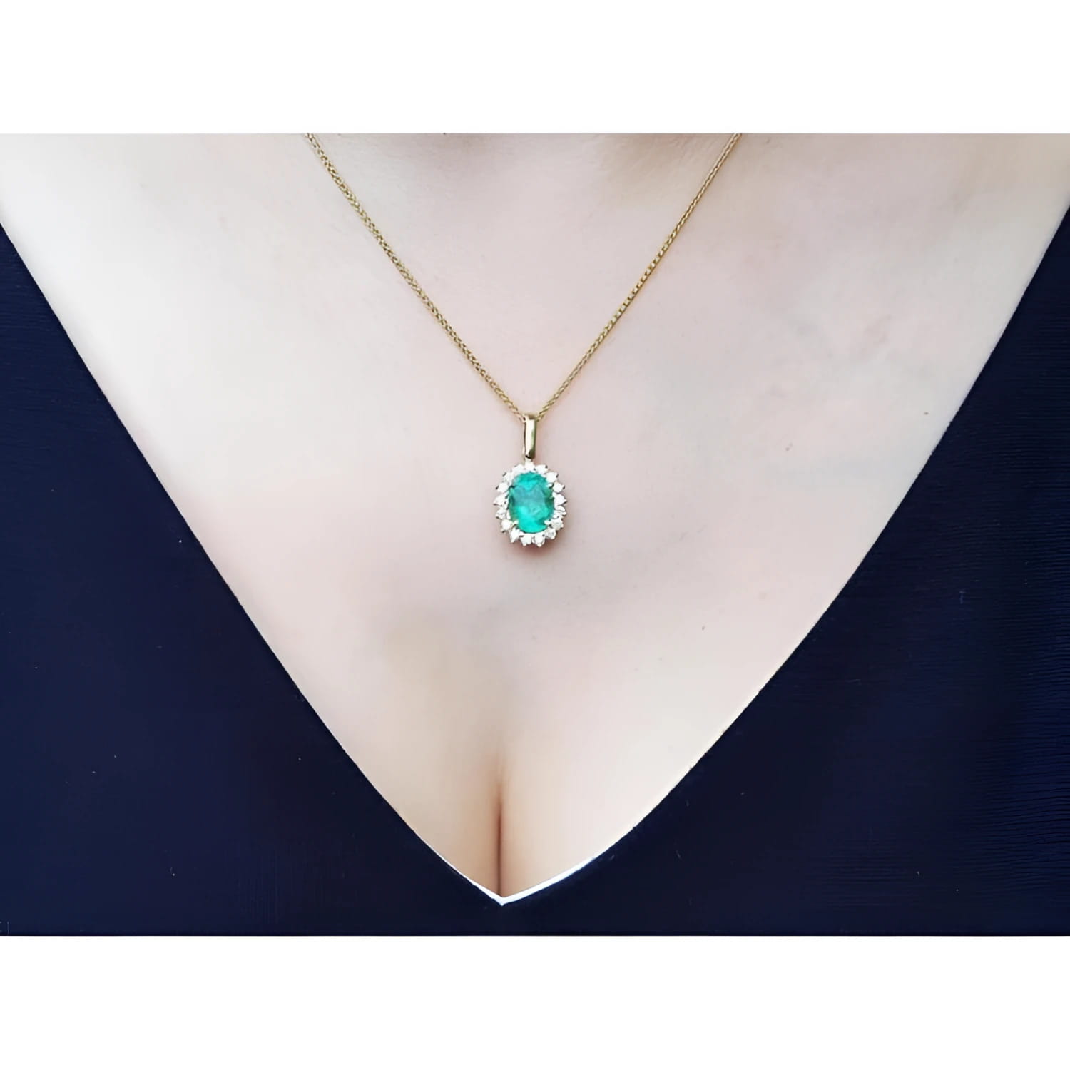 Oval natural emerald pendant with halo diamonds in 18K yellow gold on a woman's décolletage.