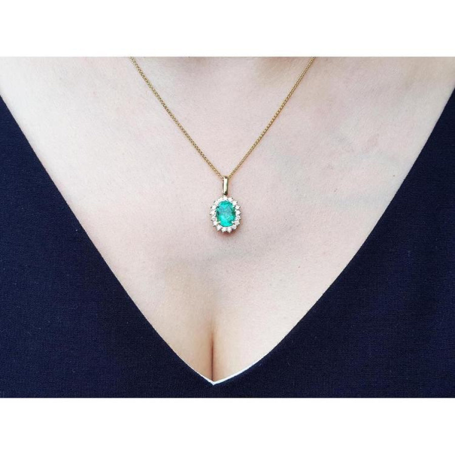 Oval natural emerald pendant with halo diamonds in 18K yellow gold on a woman's décolletage.