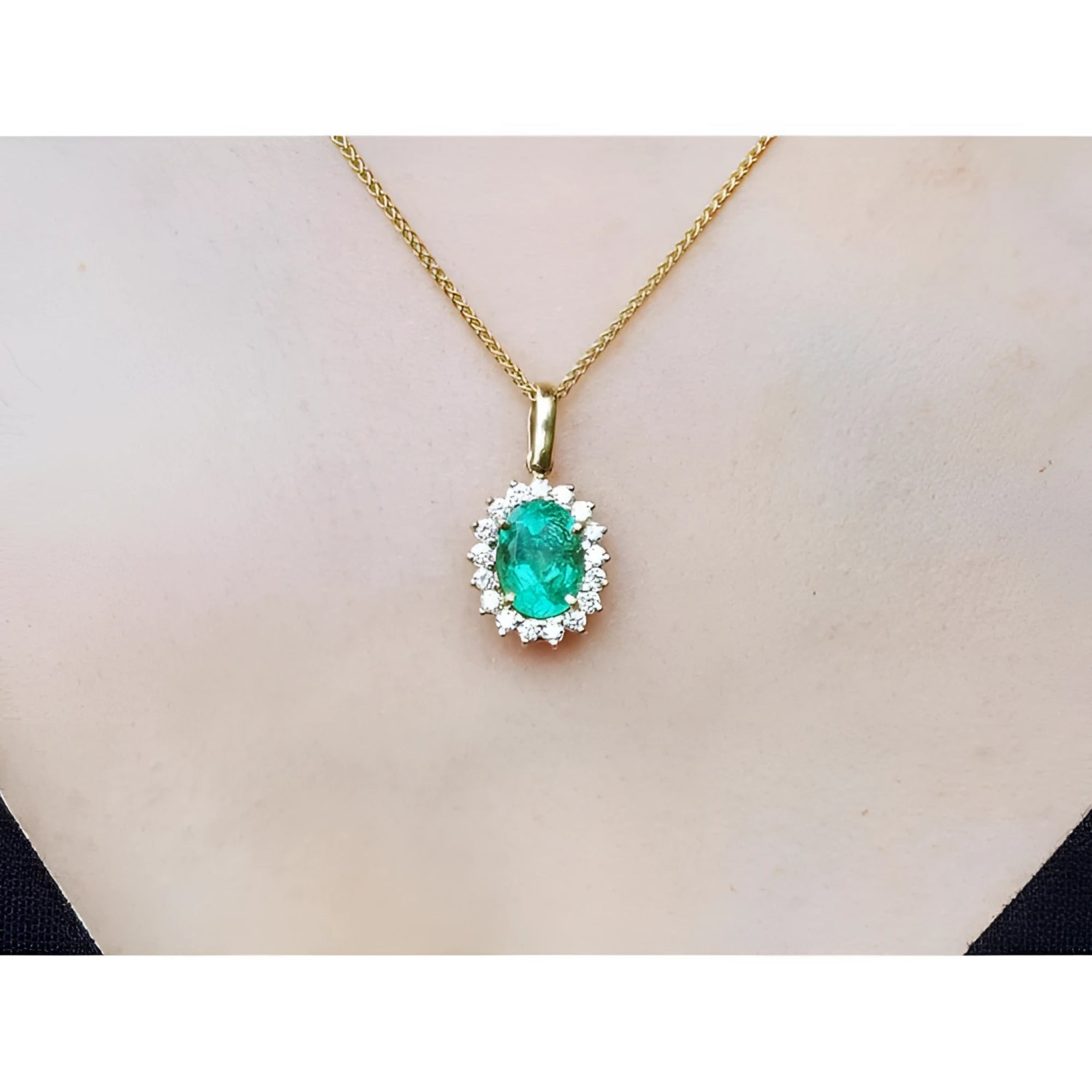 Oval 3.01 ct natural emerald pendant with halo diamonds on an 18K yellow gold chain.