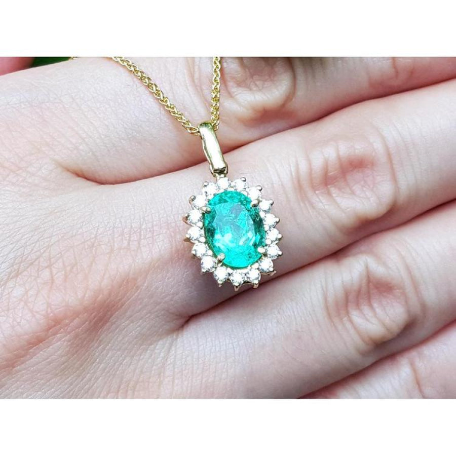 Oval natural emerald pendant with halo diamonds in 18K yellow gold, worn on a hand.