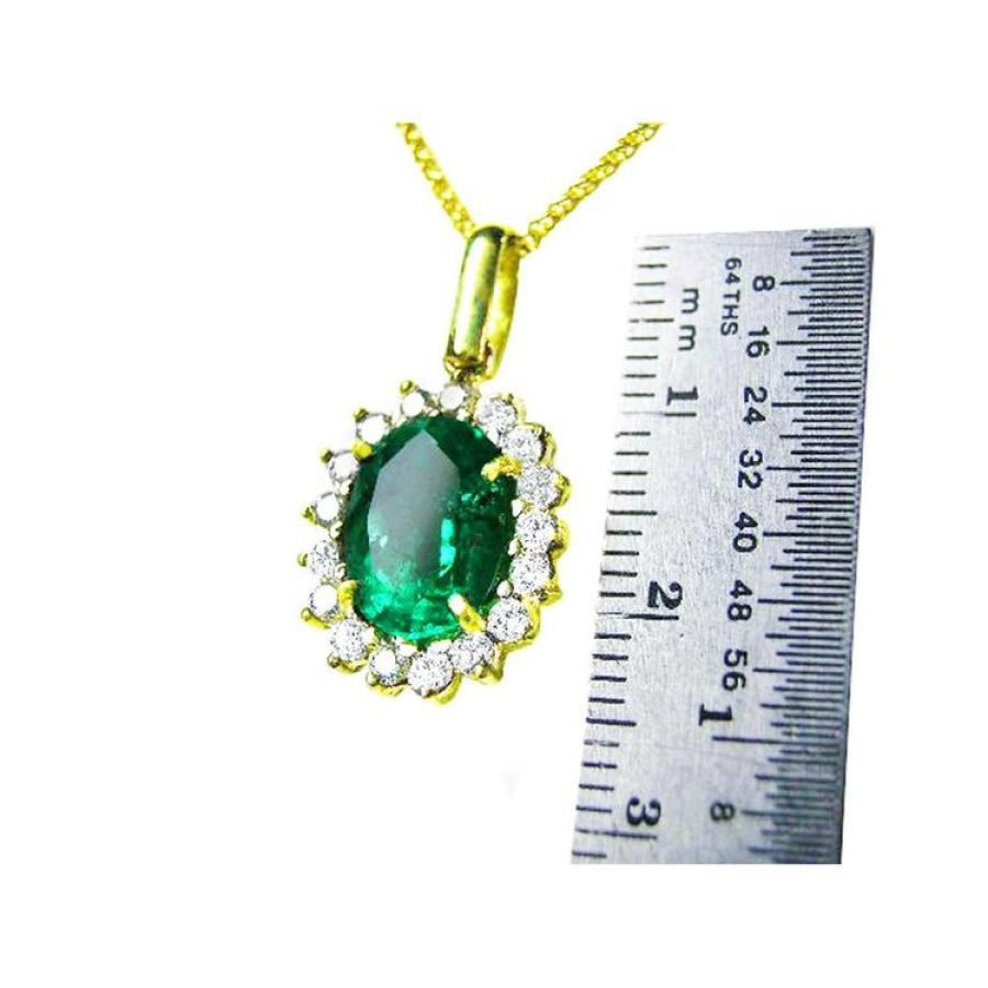 Oval natural emerald pendant with halo diamonds in 18K yellow gold, shown with a ruler for scale.