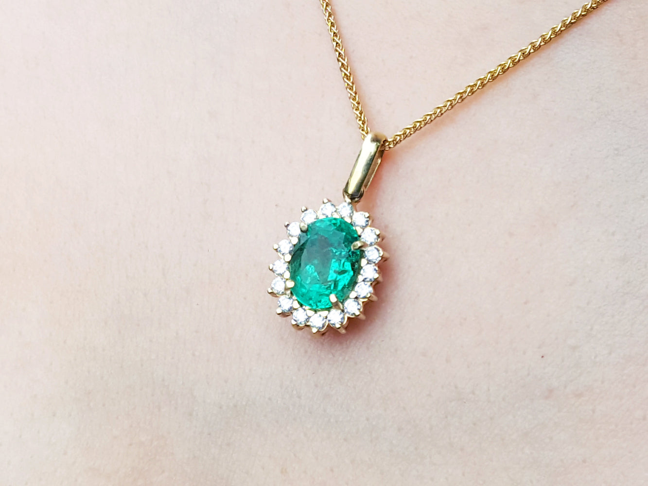 Gold necklace with an oval cut natural emerald necklace pendant on a light pink background.