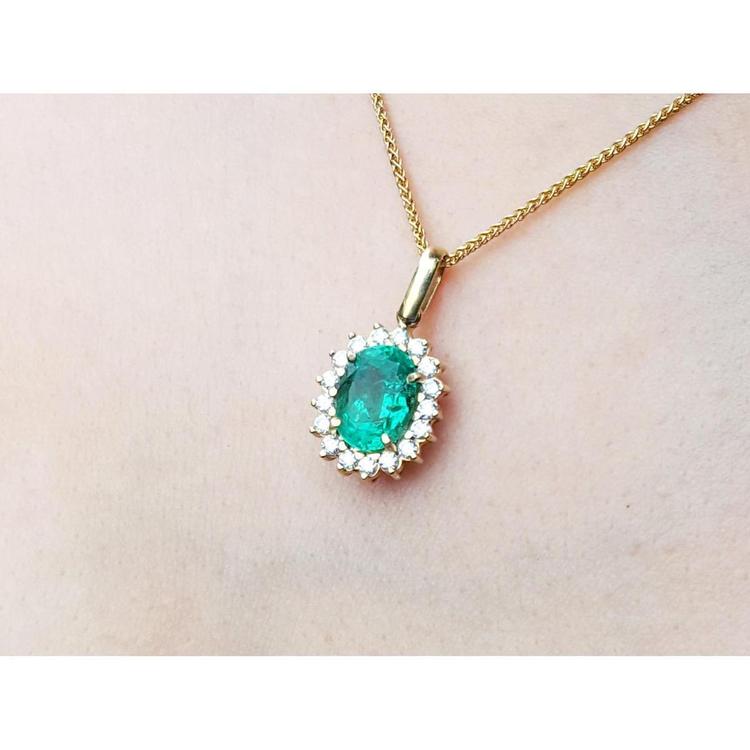 Gold necklace with an oval cut natural emerald necklace pendant on a light pink background.