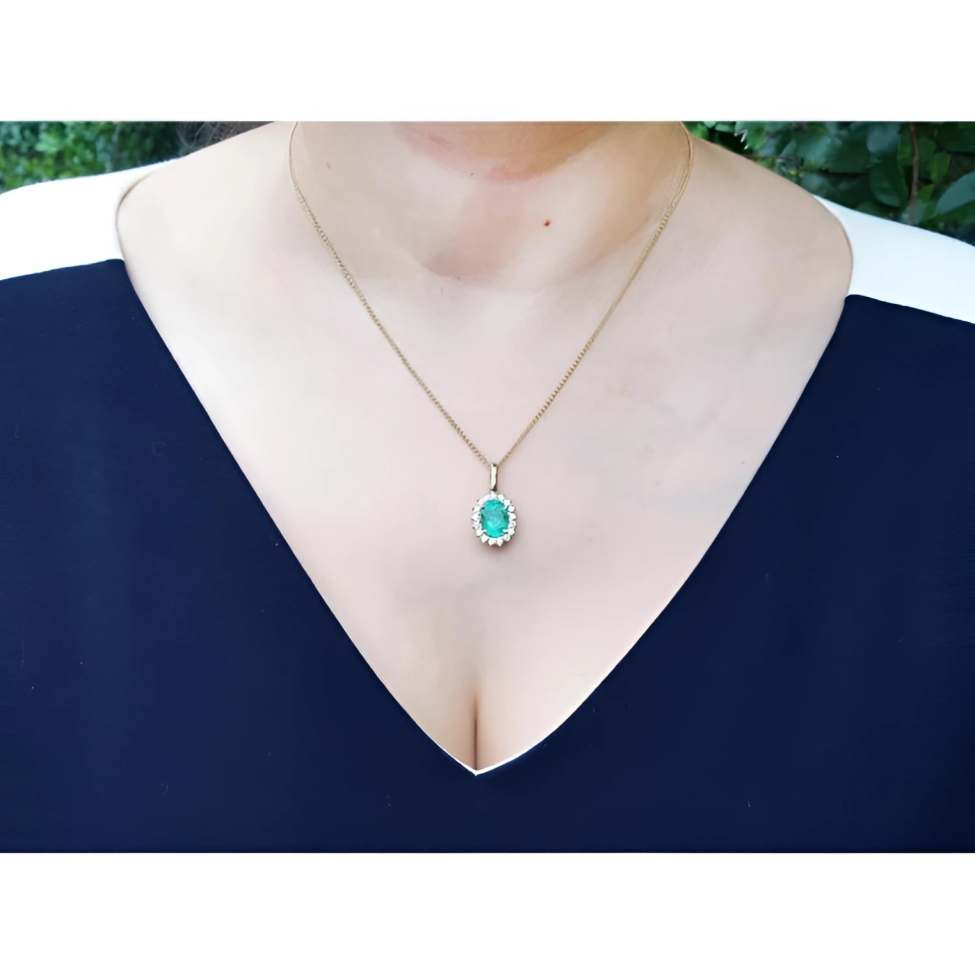 Oval natural emerald pendant with halo diamonds in 18K yellow gold, worn on a woman's neck.