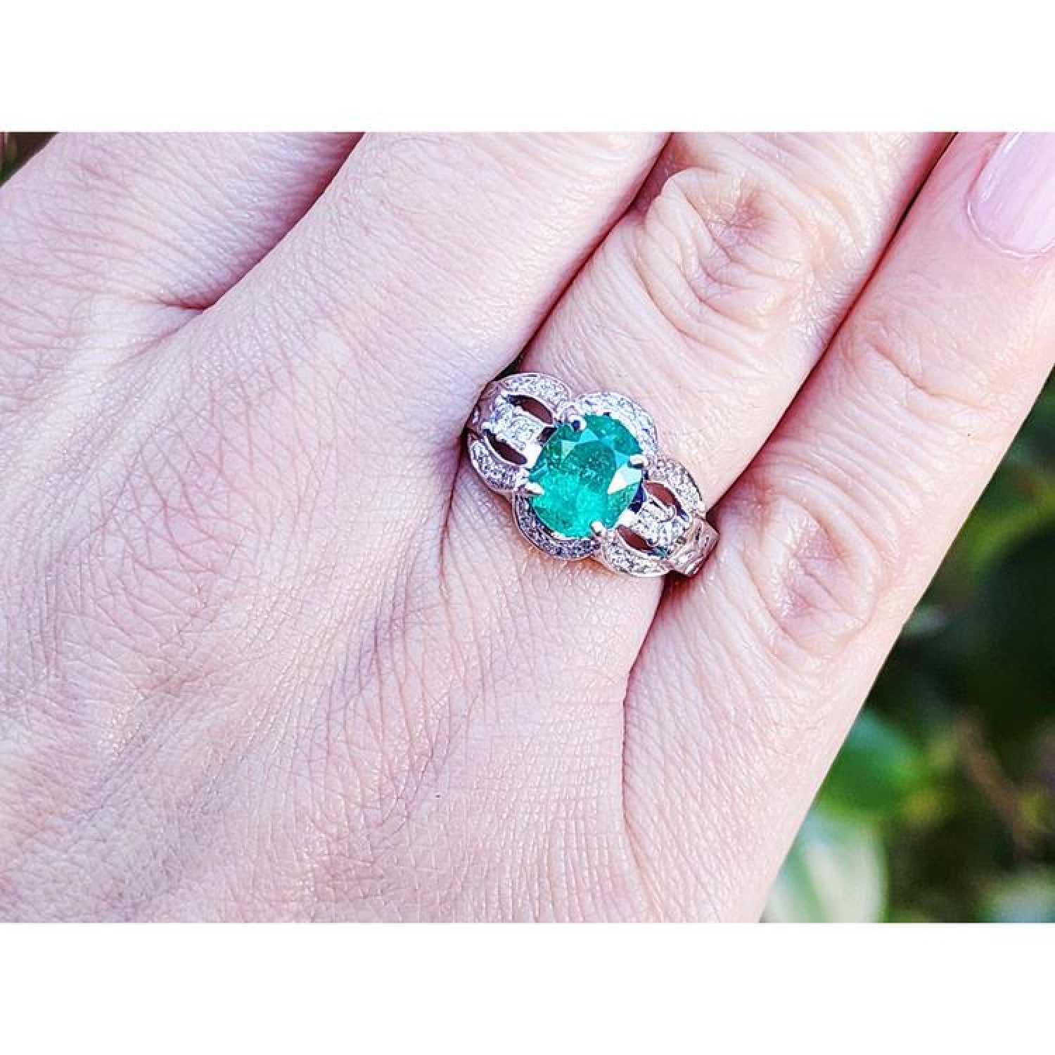 Oval emerald ring in 18K white gold with a decorative diamond band on a hand.