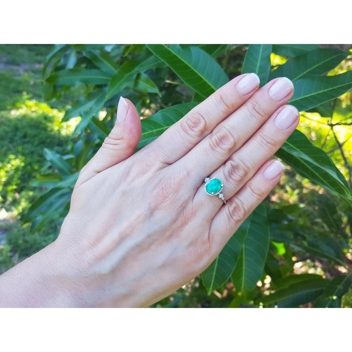 Hand wearing an oval emerald ring with leaves in the background,