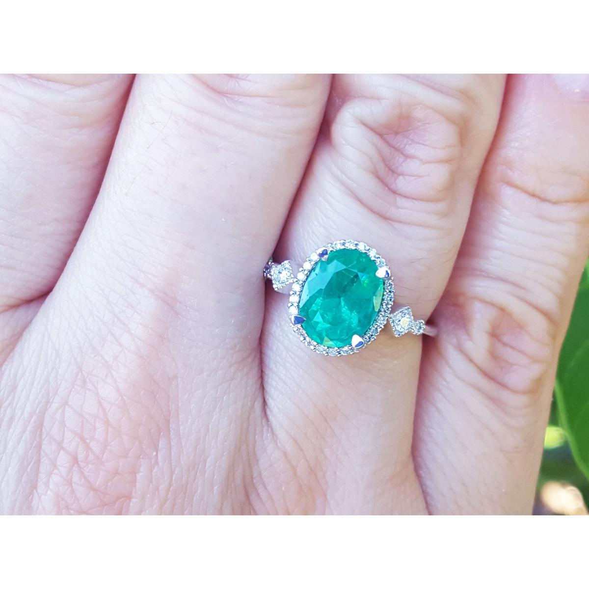 Ring with a natural emerald oval cut and accent diamonds on a person's finger.
