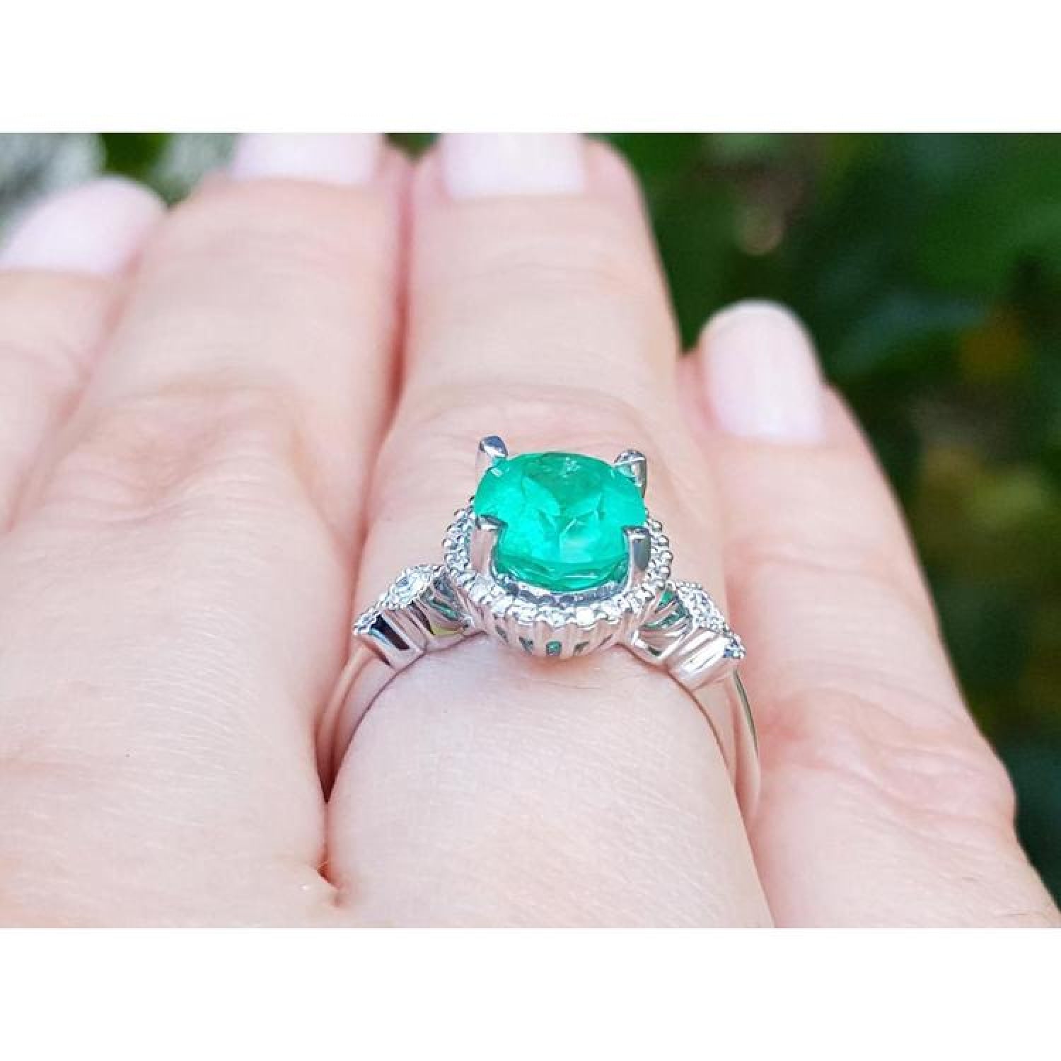 Oval 2.02 ct deep green emerald halo ring with diamonds on a 14K white gold band, worn on a finger.