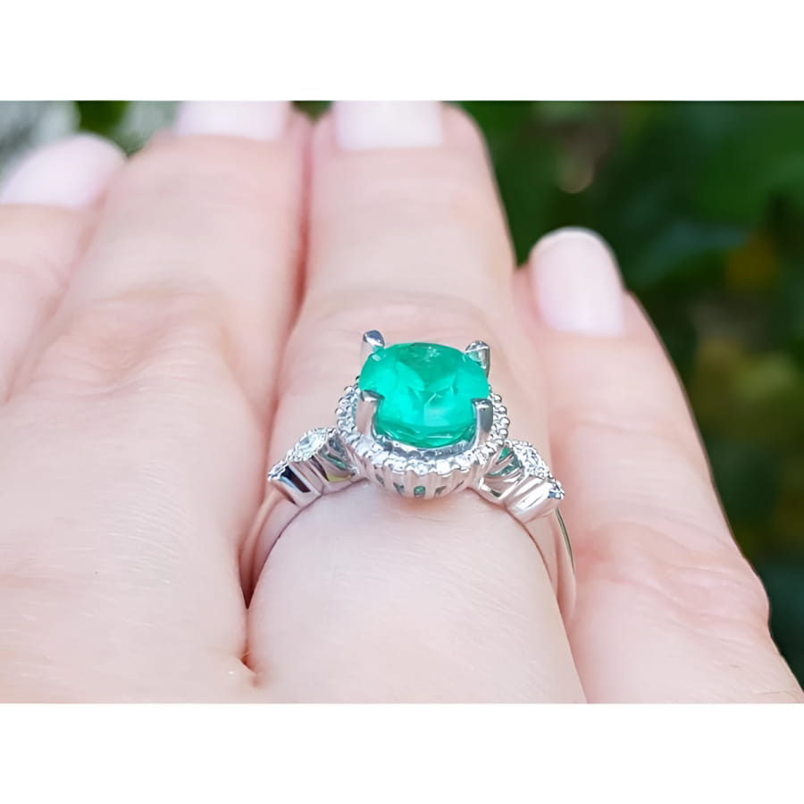 Oval 2.02 ct deep green emerald halo ring with diamonds on a 14K white gold band, worn on a finger.