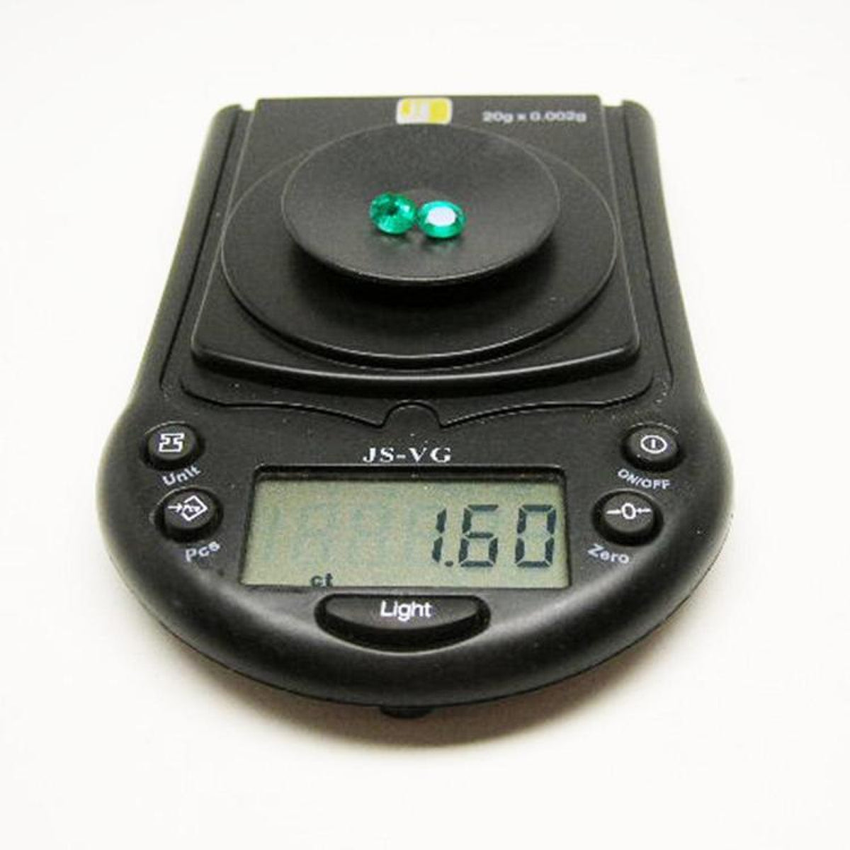Two oval-cut, deep bluish-green natural emeralds weighing 1.60 cttw on a black digital scale.