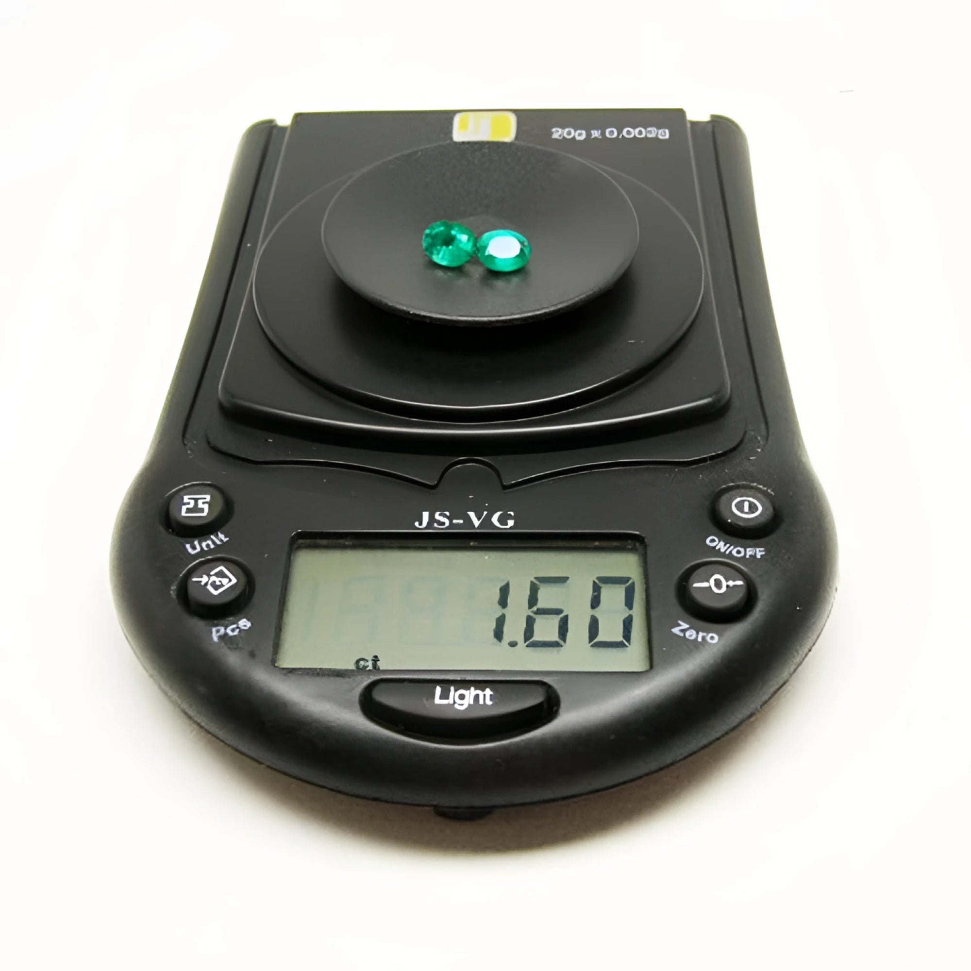 Two oval-cut, deep bluish-green natural emeralds weighing 1.60 cttw on a black digital scale.