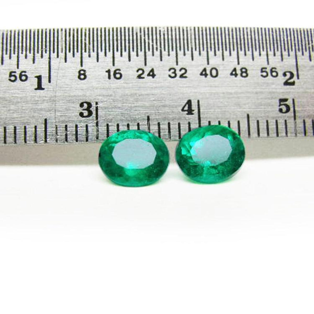 Two oval-cut natural emeralds, deep bluish-green, next to a ruler, 1.60 cttw.