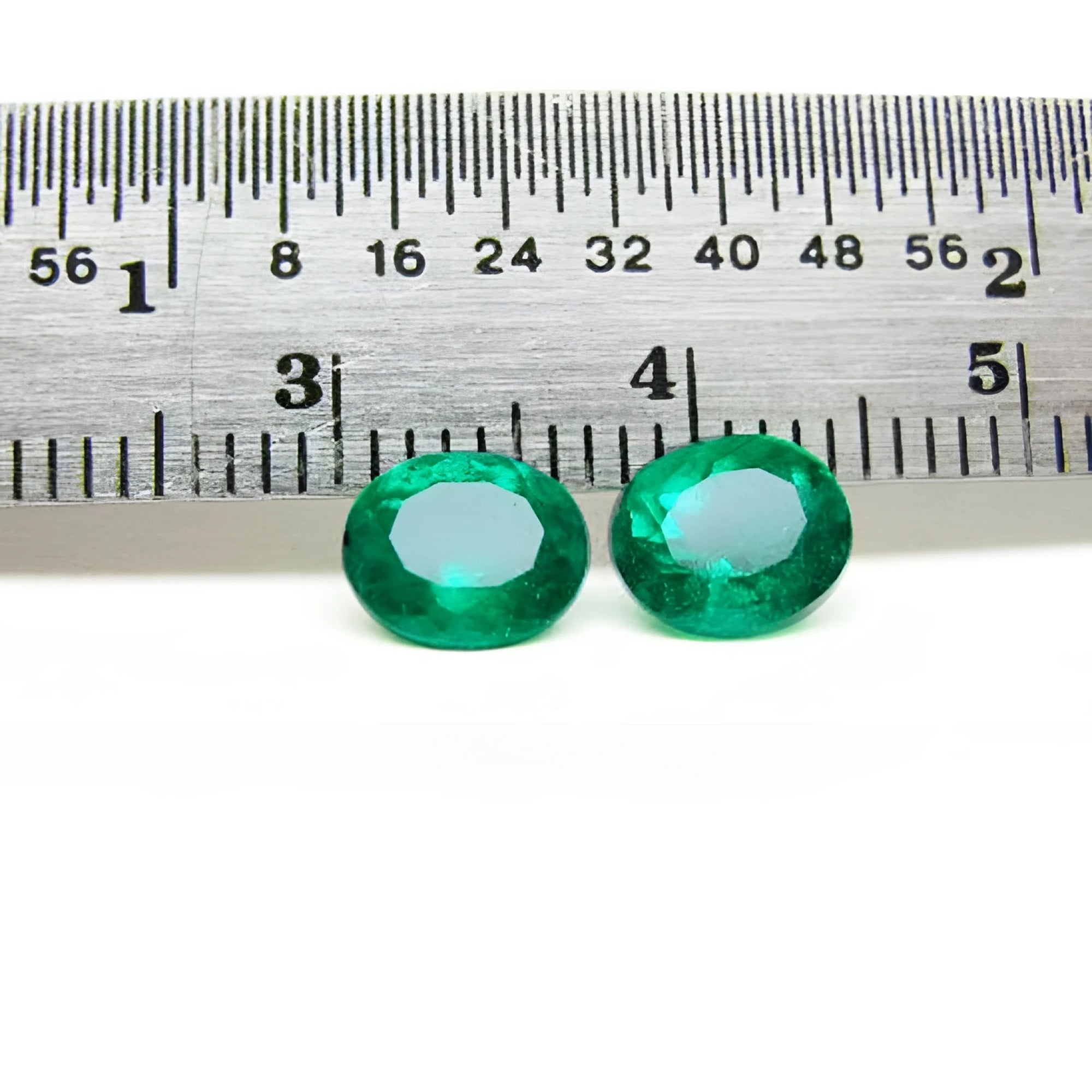 Two oval-cut natural emeralds, deep bluish-green, next to a ruler, 1.60 cttw.