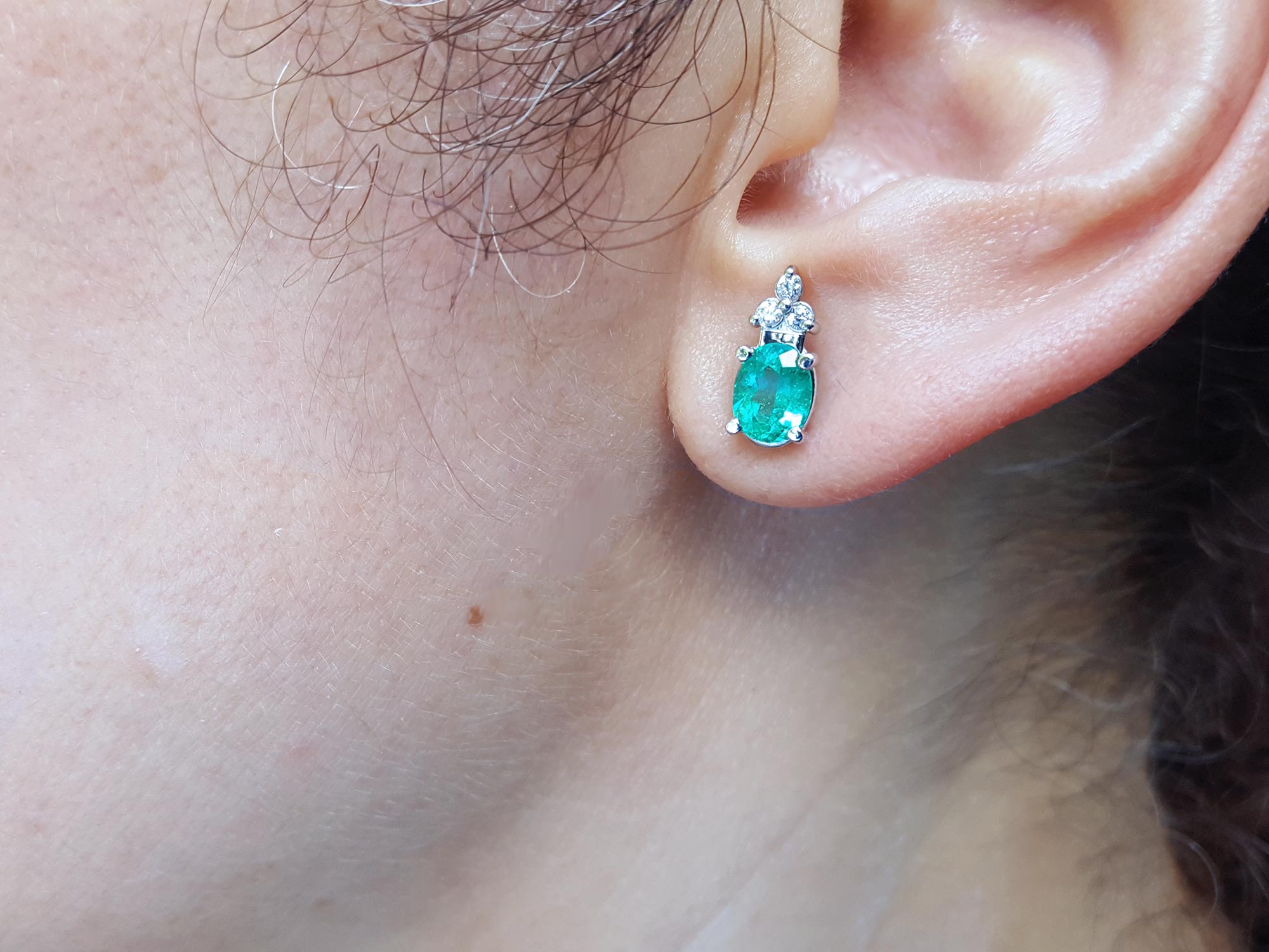 Muzo emerald earrings on a woman&#39;s ear