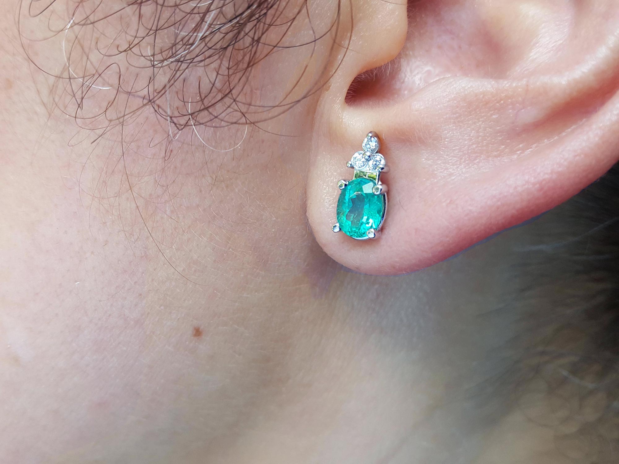 An oval cut emerald earring on a woman&#39;s earlobe left side view