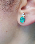 An oval cut emerald earring on a woman's earlobe left side view